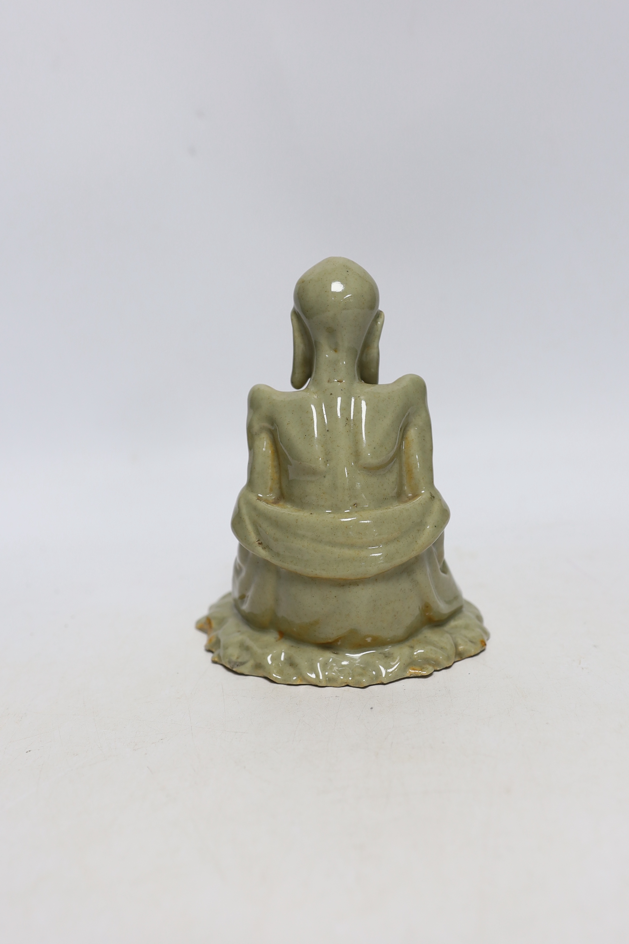 A Chinese celadon glazed figure of Laozi, 18th / 19th century, cross-legged and seated on leaves, 15cm high